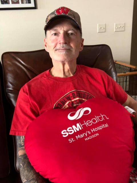 Male heart surgery patient wearing red shirt and holding red pillow on "Go Red for Women" day